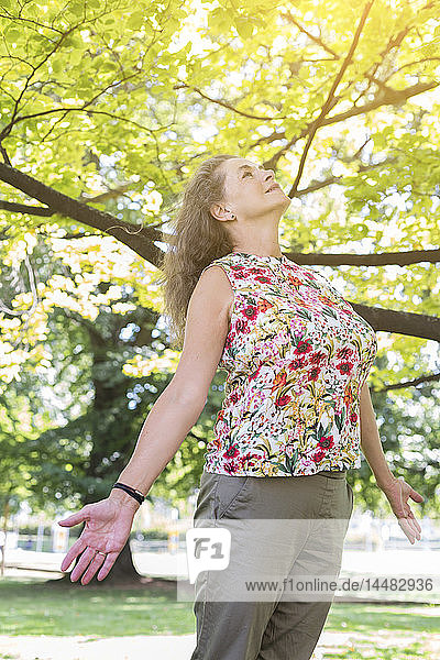 Eine reife Frau trägt ein Oberteil mit Blumendesign und entspannt sich in einem Park