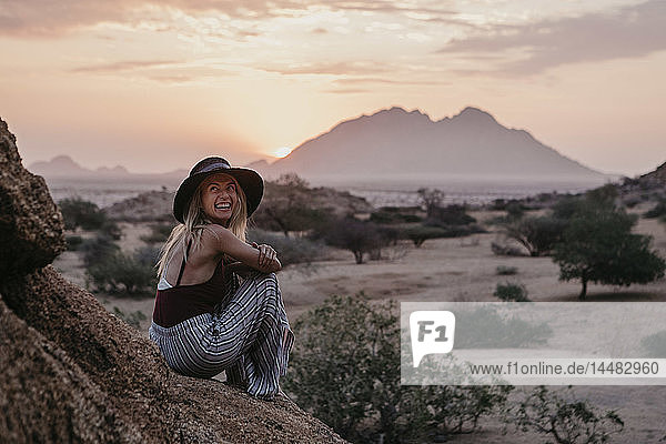 Namibia  Spitzkoppe  laughing woman sitting on a rock at sunset
