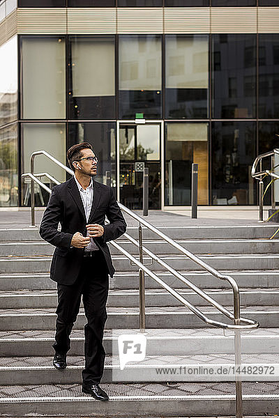 Businessman with earbuds walking on stairs in the city