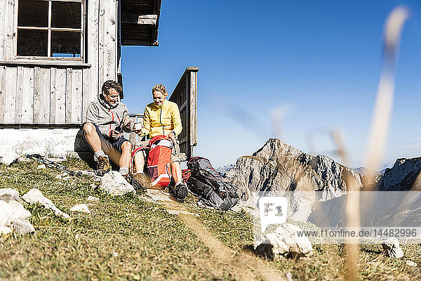 Hiking couple sitting in front of mountain hut  taking a break