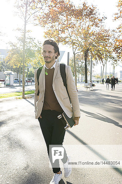 Porträt eines Mannes mit Rucksack und Skateboard in der Stadt im Herbst