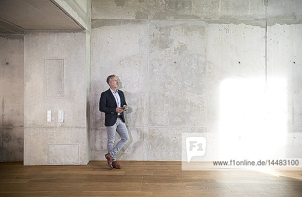 Businessman with cell phone leaning against concrete wall in a loft