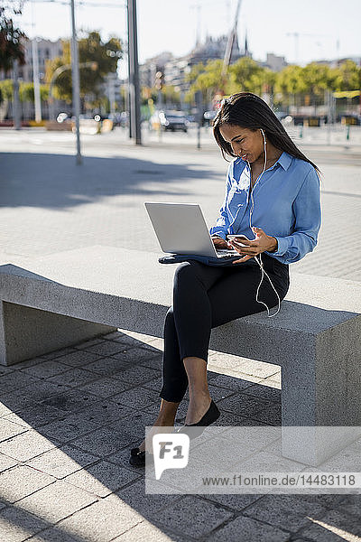 Businesswoman using laptop,  holding smartphone