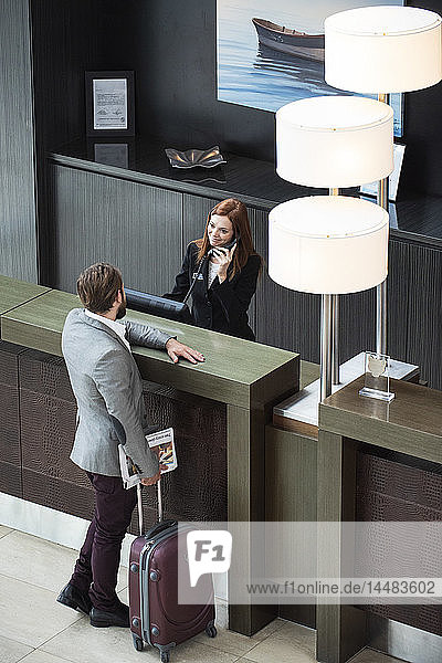 Female receptionist talking on telephone while businessman standing at counter