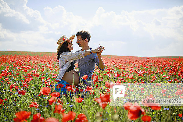 Ein schwangeres Paar tanzt in einem sonnigen  idyllischen  roten Mohnfeld