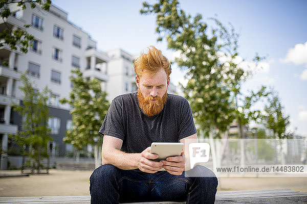 Man with beard using digital tablet on urban bench