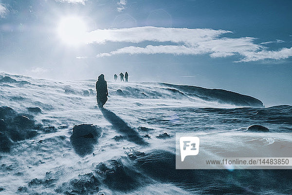 Menschen wandern durch eine sonnige  windige  schneebedeckte Landschaft  Reykjadalur  Island