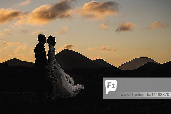 Silhouette Braut und Bräutigam küssen in der Abenddämmerung mit ruhigen Bergen im Hintergrund