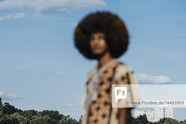 Unscharfes Porträt eines jungen Mannes mit Afro  der vor einem sonnigen blauen Himmel steht