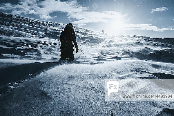 Mann geht entlang einer sonnigen  schneebedeckten Landschaft  Reykjadalur  Island