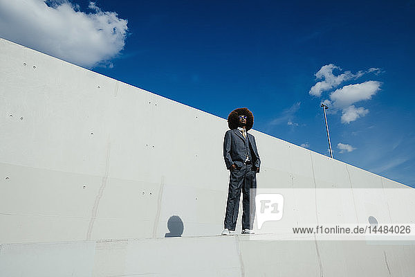 Porträt selbstbewusster  cooler  gut gekleideter junger Mann mit Afro  der an einer städtischen Wand steht