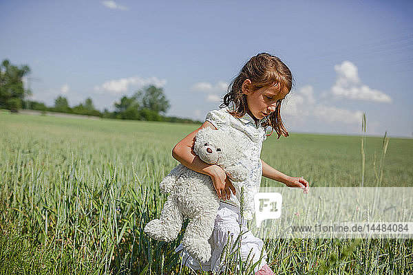 Mädchen mit Teddybär auf sonniger  grüner Wiese im ländlichen Raum