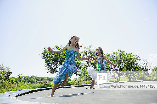 Verspielt  sorglos barfuß Mädchen in Kleidern spielen auf Trampolin in sonnigen Hinterhof