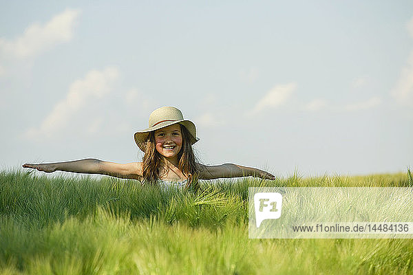 Porträt eines unbekümmerten Mädchens mit ausgestreckten Armen auf einer sonnigen  grünen Wiese