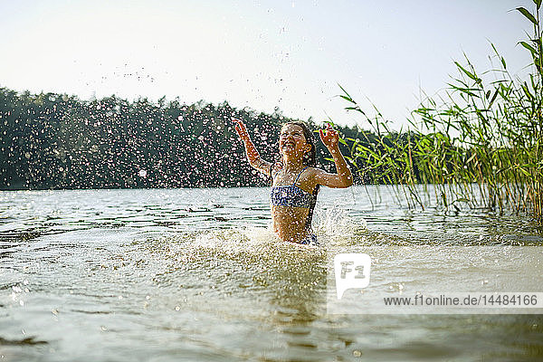 Verspieltes Mädchen planscht und schwimmt im sonnigen Sommersee