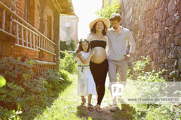 Schwangere Familie spaziert entlang eines sonnigen Bauernhauses