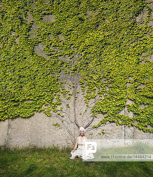 Porträt einer meditierenden Frau an einer mit Efeu überwucherten Mauer