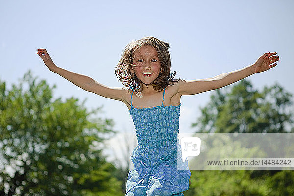 Porträt verspieltes Mädchen mit ausgestreckten Armen  das im sonnigen Hof vor Freude springt