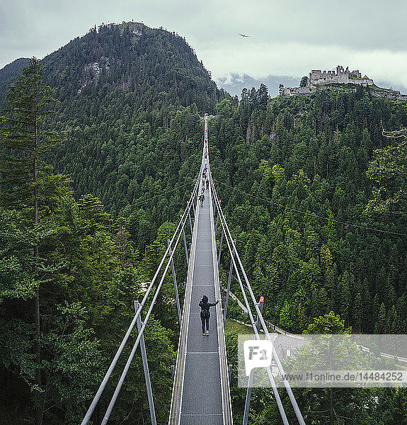 People walking across suspension bridge over green treetops  Tyrol  Austria