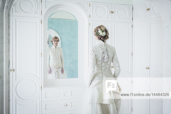Elegante Braut im Spitzenhochzeitskleid am Spiegel