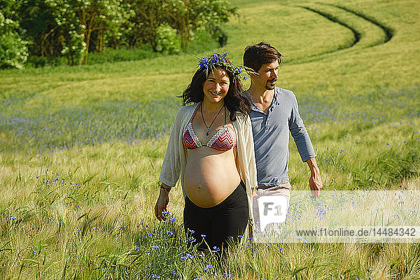 Portrait happy pregnant couple walking in sunny  idyllic rural field with wildflowers