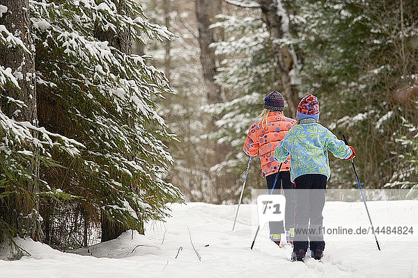 Zwei junge Mädchen beim Skilanglauf auf einer Loipe durch Fichtenwälder im Winter in Ely  Minnesota