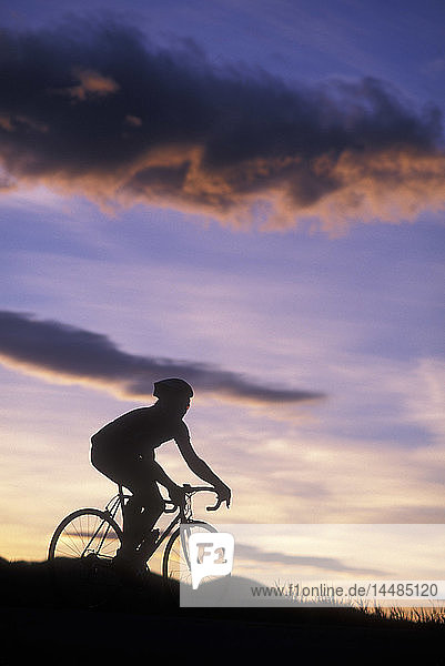 Silhouette of a road biker riding against a colorful sunset sky