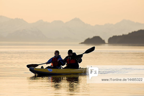Sea Kayakers paddle the shoreline on a calm evening at sunset in Favorite Passage near Juneau  Alaska with Eagle Peak & Admiralty Island in the background