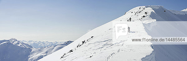 Ein Backcountry-Skifahrer und ein Snowboarder bahnen sich ihren Weg über einen verschneiten Bergrücken am Hatcher Pass in Süd-Zentral-Alaska