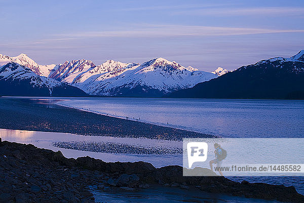 Hiker at dusk on ridge overlooking Turnagain Arm with sun setting on Chugach Mountains in Southcentral Alaska