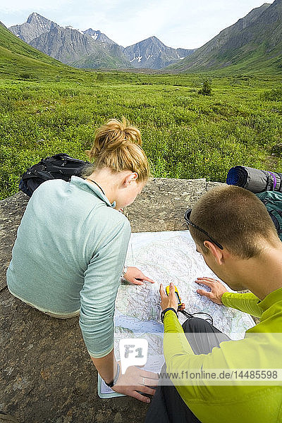 Male & female hikers looking at map while resting on rock in Chugach State Park Alaska Summer