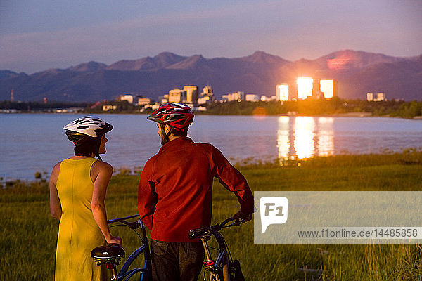 Radfahrer  die sich ausruhen und den Sonnenuntergang entlang des Tony Knowles Coastal Trail mit der Skyline von Anchorage im Hintergrund genießen  Southcentral Alaska