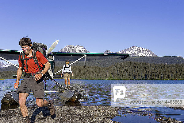 People leap from floatplane to shoreline on lake to go hiking Kenai Mtns Kenai Peninsula Alaska Summer