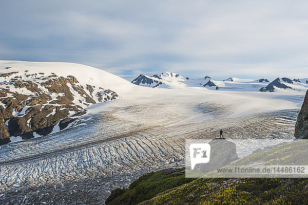 Silhouette eines Mannes  der auf einem Felsen steht und den Blick auf den Exit Glacier und das Harding Ice Feild genießt  Kenai Fjords National Park  Southcentral Alaska