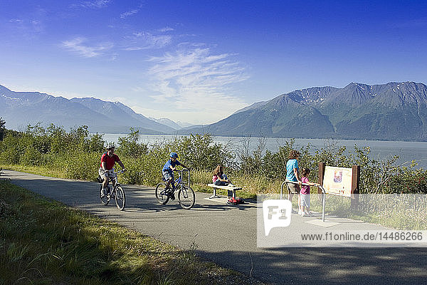 Family reads info sign on Coastal Trail near Indian  AK  while bicyclists ride by. SC Alaska Summer.