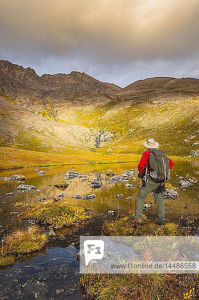 Ein Wanderer hält an einem Herbsttag in Süd-Zentral-Alaska an  um sich den Lower Hidden Lake im Chugach State Park anzusehen.