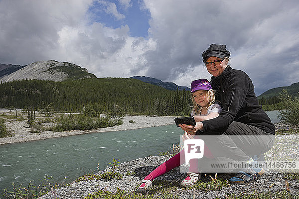 Mother and daughter take a selfie alongside the Toad River  Muncho Lake Provincial Park  British Columbia  Canada  summer