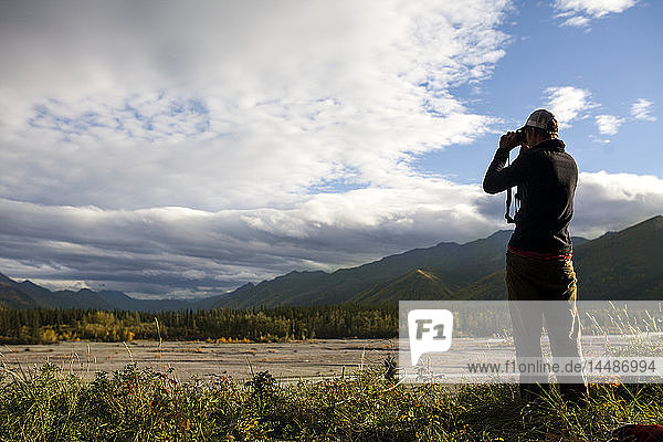 Mann beobachtet ein verzweigtes Flussbett mit einem Fernglas bei der Jagd in der Nähe von Tok  Süd-Zentral-Alaska