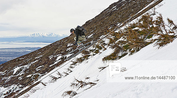 Ein Skitourengeher schnappt beim Skifahren zwischen Sträuchern auf der Seite von Peak 3 in der Nähe von Anchorage,  Alaska,  während des Frühlings ein wenig Luft.