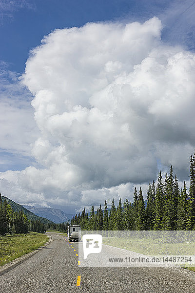 RV driving on the Alaska Highway with cumulonimbus clouds overhead  west of Fort Nelson  British Columbia  Canada  Summer