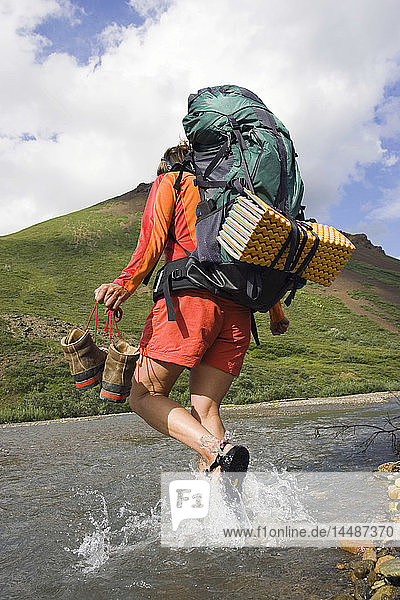 Backpacker carrying shoes while crossing Stony Creek Denali National Park Interior Alaska Summer