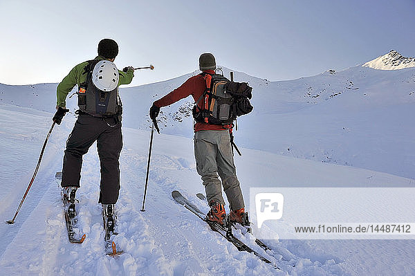 A backcountry skier points out a peak to another skier while taking a break in Hatcher Pass  Southcentral  Alaska