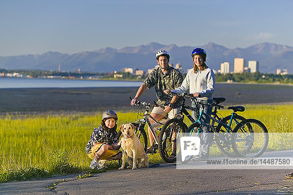 Family w/pet companion riding bicycles on Tony Knowles Coastal Trail Anchorage Alaska Summer