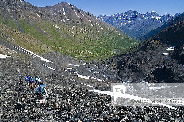 A group of backpackers make their way downhill away from Raven Glacier in Crow Pass  Chugach State Park  Southcentral Alaska  Summer