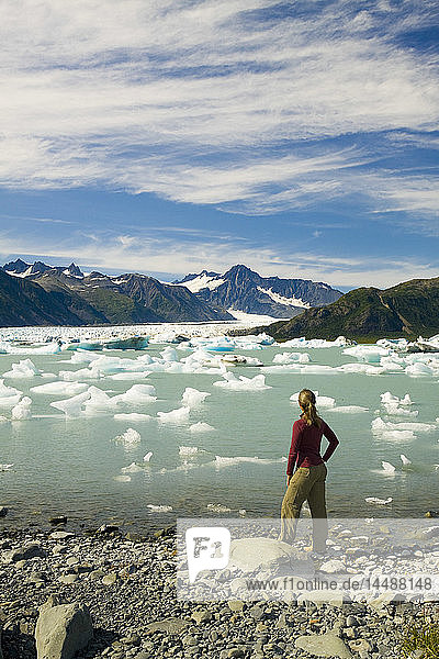 Female hiker pauses to view Bear Glacier from the shore of Bear Glacier Lake in Kenai Fjords National Park  Kenai Peninsula  Southcentral Alaska  Summer