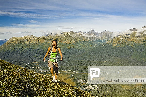 Junge erwachsene hispanische Frau beim Wandern auf dem Gipfel des Berges Alyeska mit Blick auf die Chugach Mountains und das Girdwood Valley in Süd-Zentral-Alaska