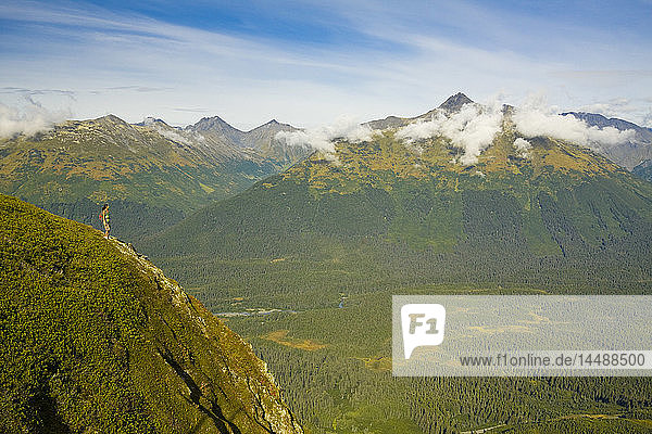 Young adult Hispanic woman hiking on top of Mt. Alyeska with view of Chugach Mountains & Girdwood Valley in Southcentral Alaska