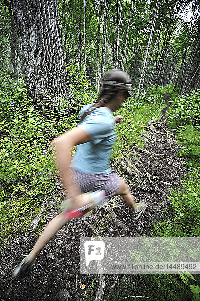 Woman runs over tree roots on the Dew Mound Trail along Eagle River in Chugach State Park in Southcentral Alaska