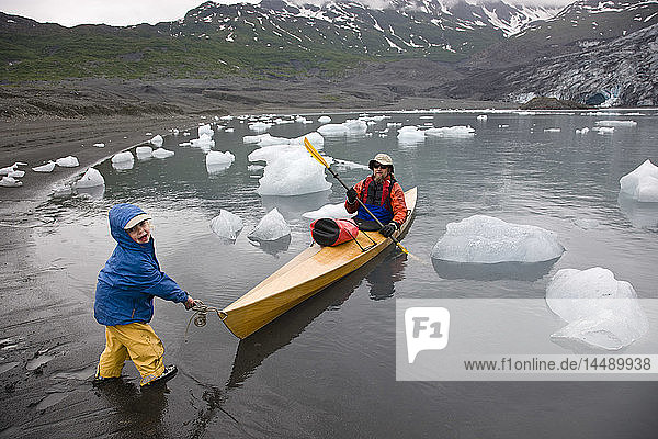 Young child helps pull in kayak as father finishes kaying in Shoup Bay State Marine Park  Prince William Sound  Southcentral Alaska