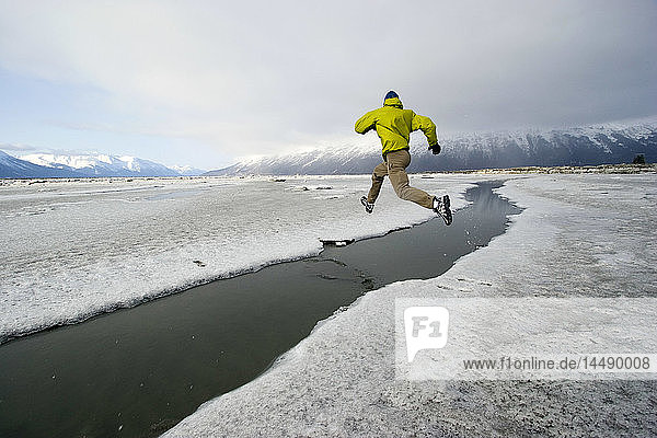 Man runs along Turnagain Arm on crumbly ice slush and mud surface in the winter near Girdwood Alaska